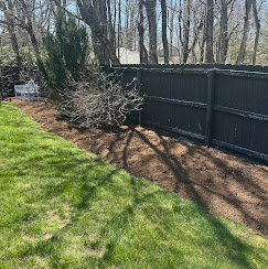 Freshly mulched garden bed along a black wooden privacy fence with a healthy green lawn.